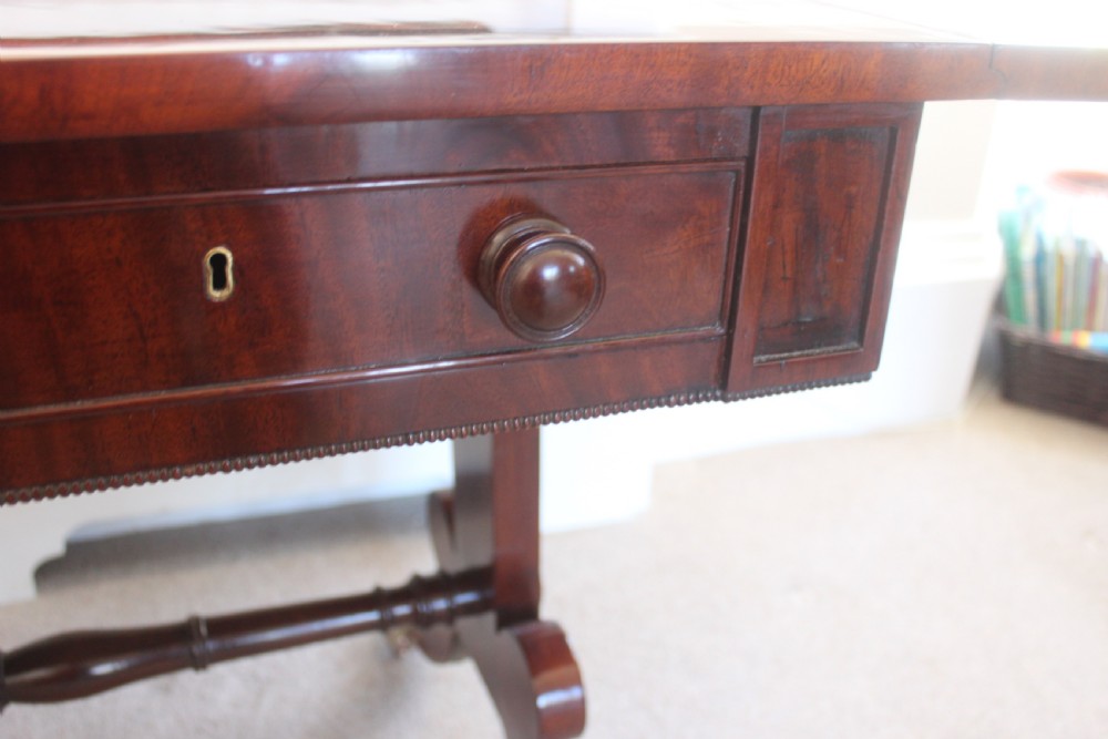 An early nineteenth-century mahogany sofa table featuring two drop leaves, two frieze drawers with knob handles, a turned central stretcher, and splayed legs with brass paw feet and castors. View XIII