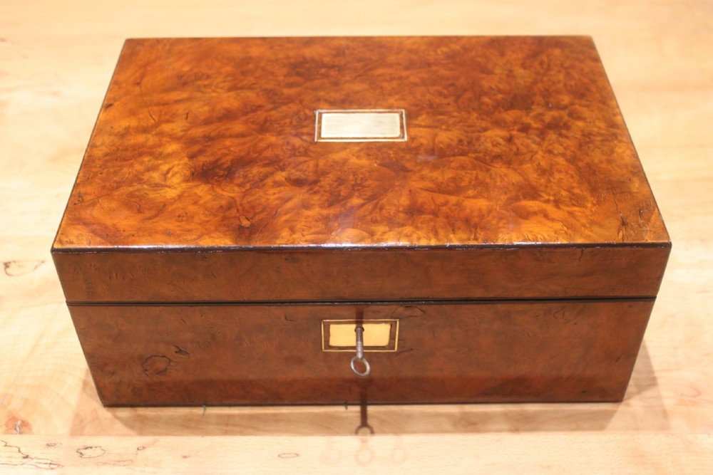 A rectangular Victorian burr walnut writing slope featuring a brass cartouche on top and a brass escutcheon with key on the front.