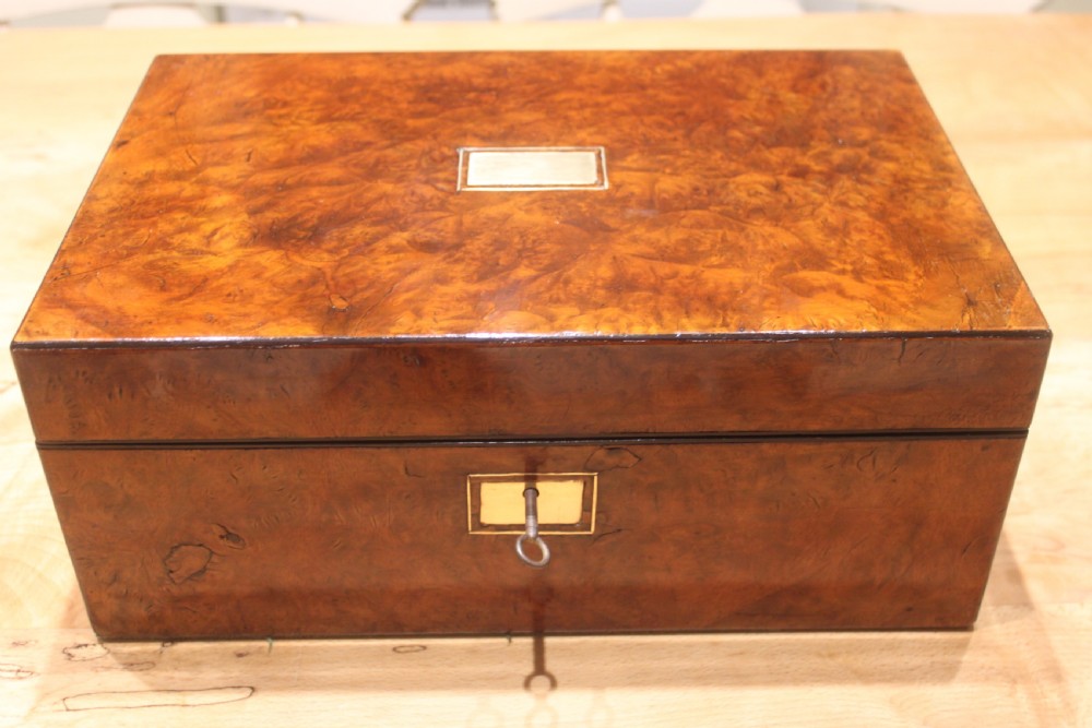 A rectangular Victorian burr walnut writing slope featuring a brass cartouche on top and a brass escutcheon with key on the front. View II