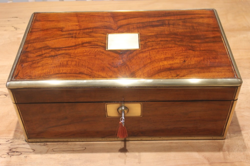 A rectangular Victorian walnut writing slope featuring brass bound corners, a central rectangular brass cartouche, and a key inserted into the front keyhole plate.