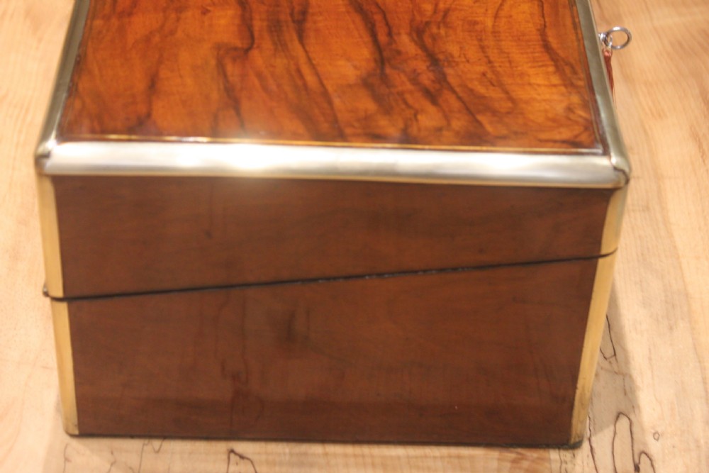A rectangular Victorian walnut writing slope featuring brass bound corners, a central rectangular brass cartouche, and a key inserted into the front keyhole plate. View II