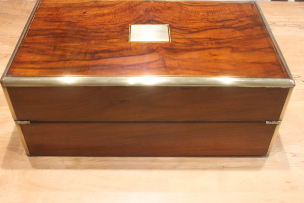 A rectangular Victorian walnut writing slope featuring brass bound corners, a central rectangular brass cartouche, and a key inserted into the front keyhole plate. View III