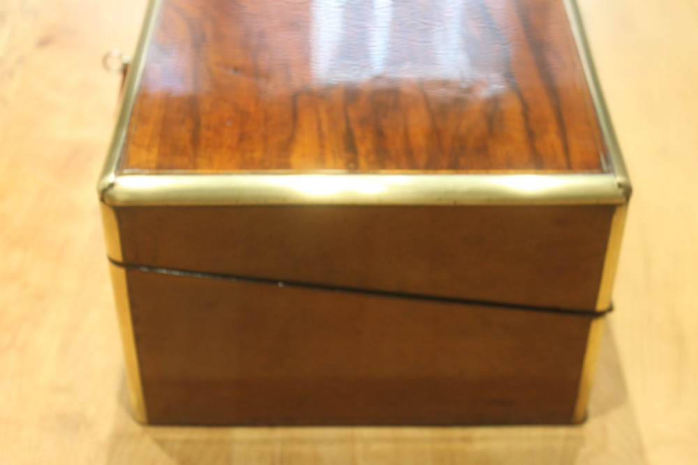 A rectangular Victorian walnut writing slope featuring brass bound corners, a central rectangular brass cartouche, and a key inserted into the front keyhole plate. View IV