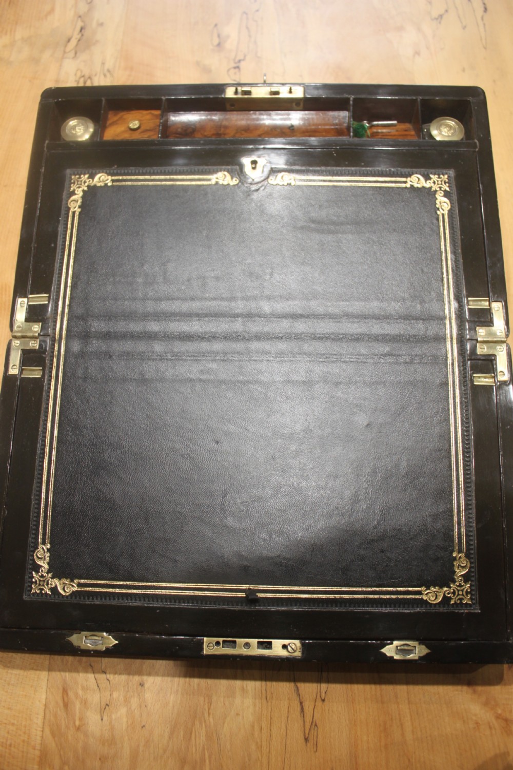 A rectangular Victorian walnut writing slope featuring brass bound corners, a central rectangular brass cartouche, and a key inserted into the front keyhole plate. View V