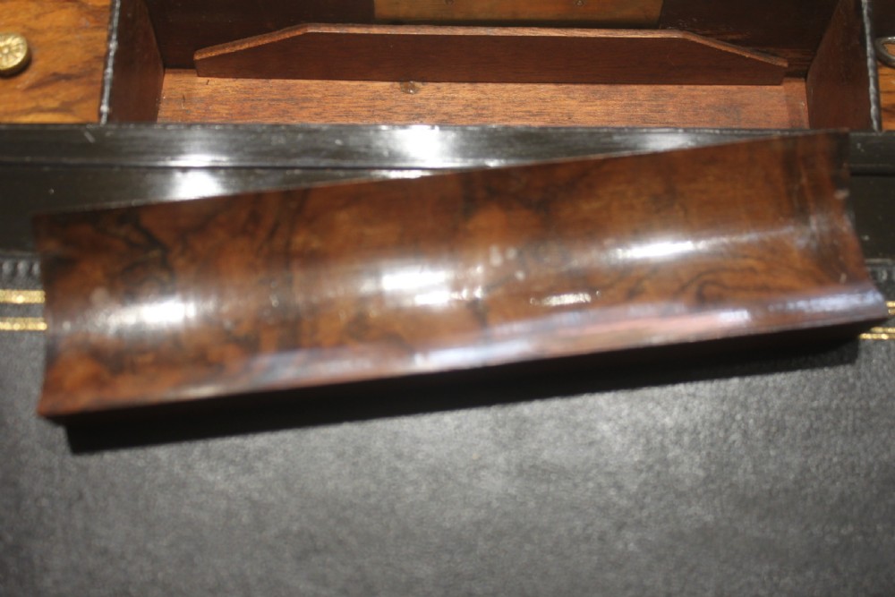 A rectangular Victorian walnut writing slope featuring brass bound corners, a central rectangular brass cartouche, and a key inserted into the front keyhole plate. View IX