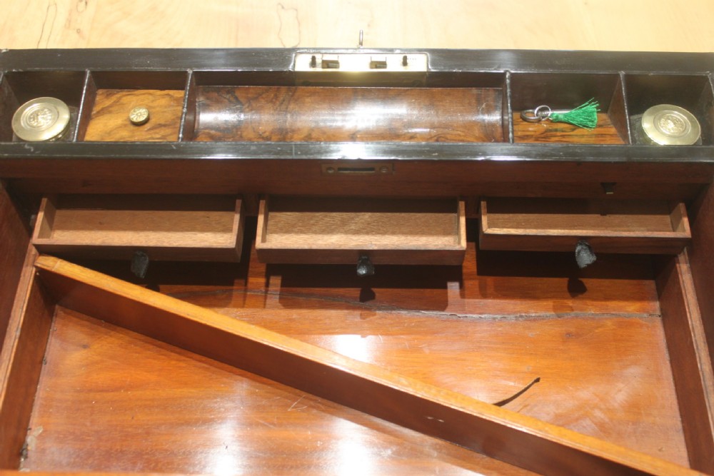 A rectangular Victorian walnut writing slope featuring brass bound corners, a central rectangular brass cartouche, and a key inserted into the front keyhole plate. View XII