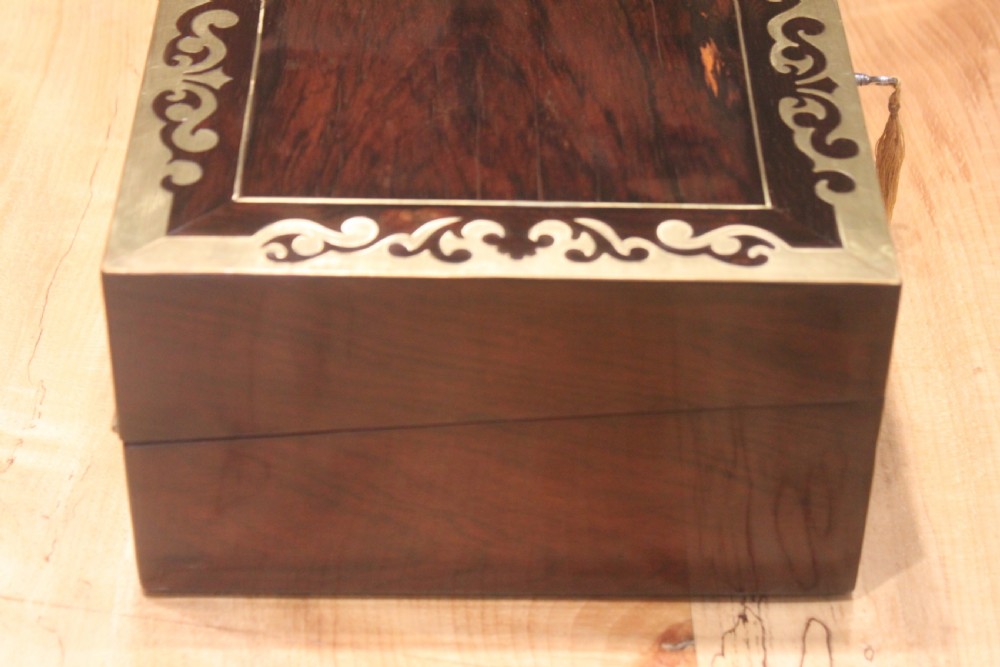 A rectangular dark rosewood box decorated with intricate brass scrollwork inlay along the borders and top centre, complete with a key inserted into the front lock. View III