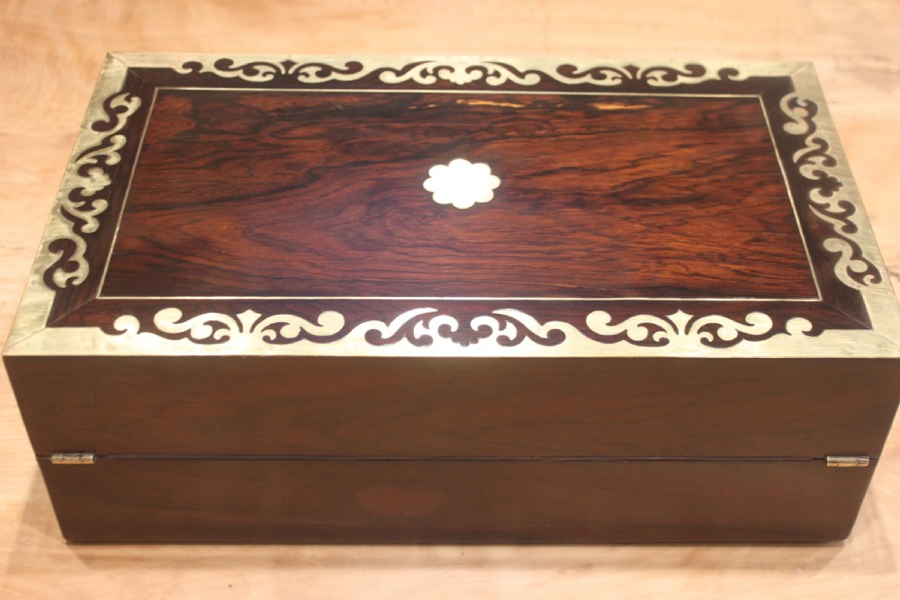 A rectangular dark rosewood box decorated with intricate brass scrollwork inlay along the borders and top centre, complete with a key inserted into the front lock. View IV