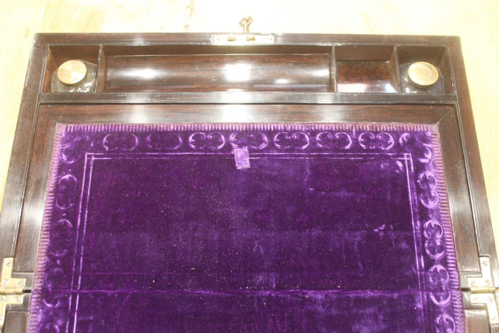 A rectangular dark rosewood box decorated with intricate brass scrollwork inlay along the borders and top centre, complete with a key inserted into the front lock. View VIII