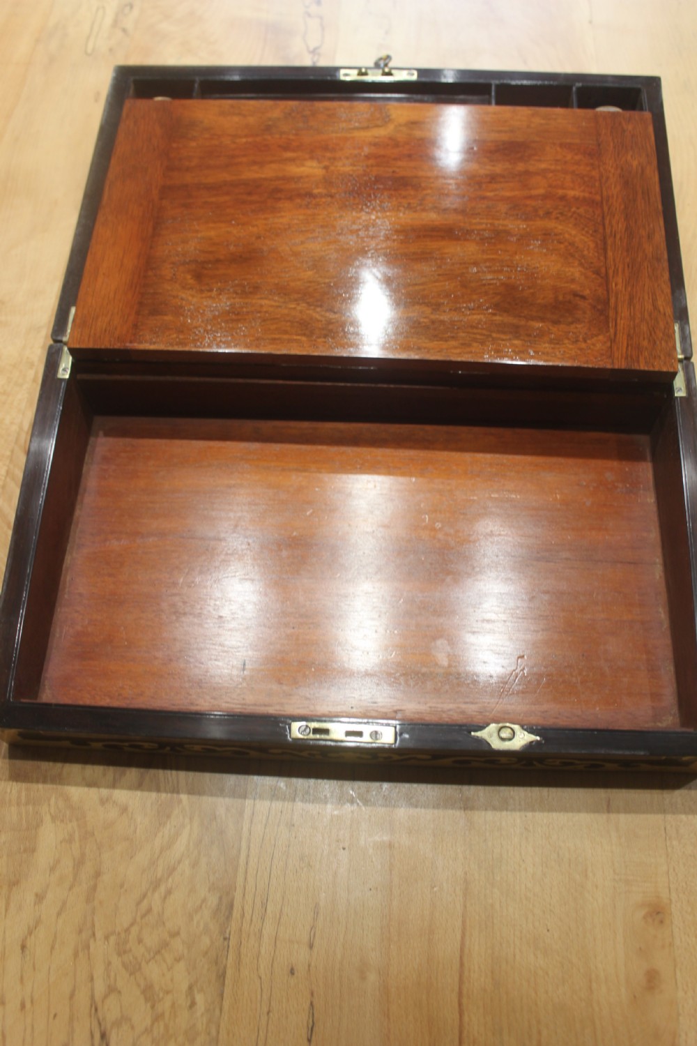A rectangular dark rosewood box decorated with intricate brass scrollwork inlay along the borders and top centre, complete with a key inserted into the front lock. View IX