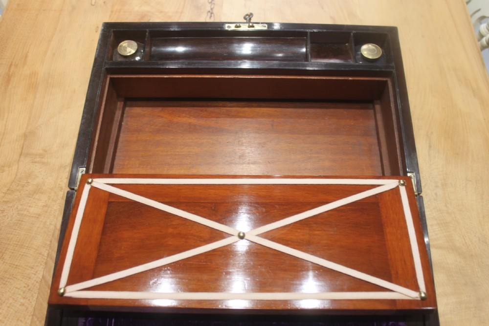 A rectangular dark rosewood box decorated with intricate brass scrollwork inlay along the borders and top centre, complete with a key inserted into the front lock. View X