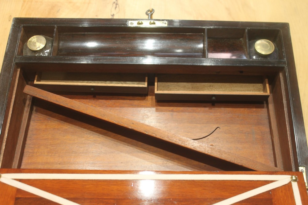 A rectangular dark rosewood box decorated with intricate brass scrollwork inlay along the borders and top centre, complete with a key inserted into the front lock. View XI