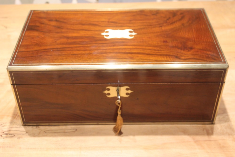A rectangular dark walnut box featuring brass corner edging, an inlaid brass cartouche on the lid, and a brass escutcheon with a key and tassel.