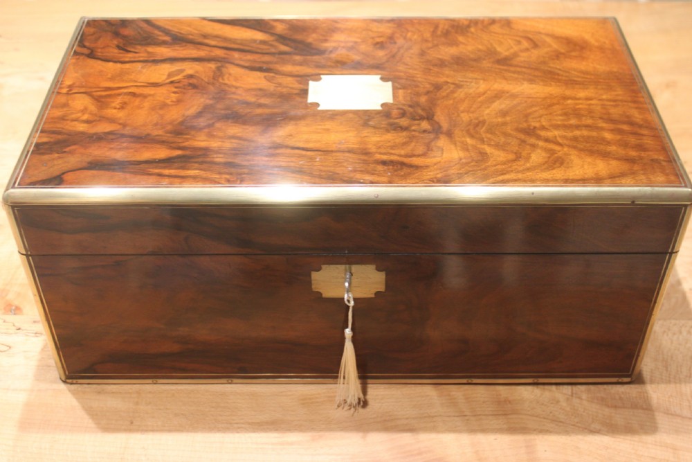 A rectangular Victorian writing slope crafted from figured walnut with brass binding, a top brass cartouche, and a brass key escutcheon with a tassel.