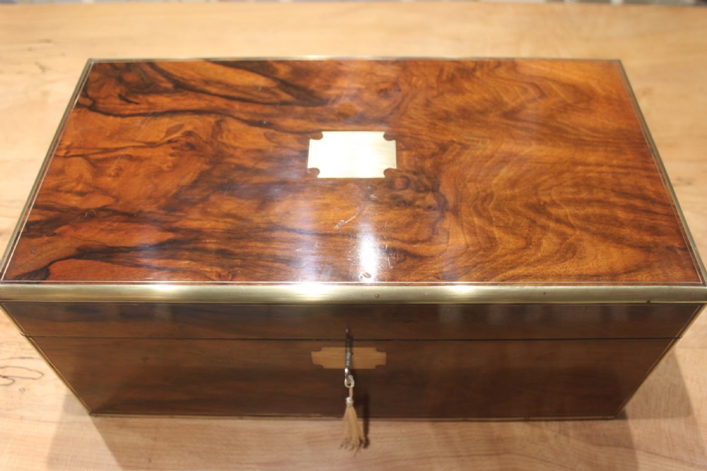 A rectangular Victorian writing slope crafted from figured walnut with brass binding, a top brass cartouche, and a brass key escutcheon with a tassel. View II