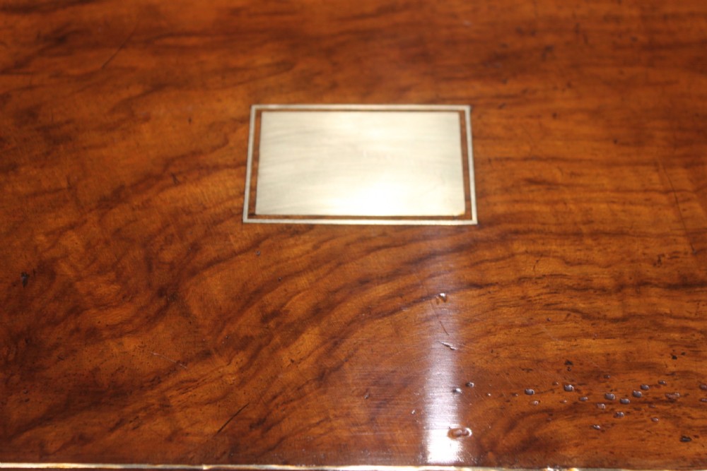 A closed Victorian writing slope crafted from figured walnut veneer featuring brass edging, line inlay, a brass cartouche, and a key inserted in the Bramah lock with a tassel. View II