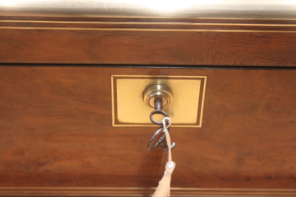 A closed Victorian writing slope crafted from figured walnut veneer featuring brass edging, line inlay, a brass cartouche, and a key inserted in the Bramah lock with a tassel. View III