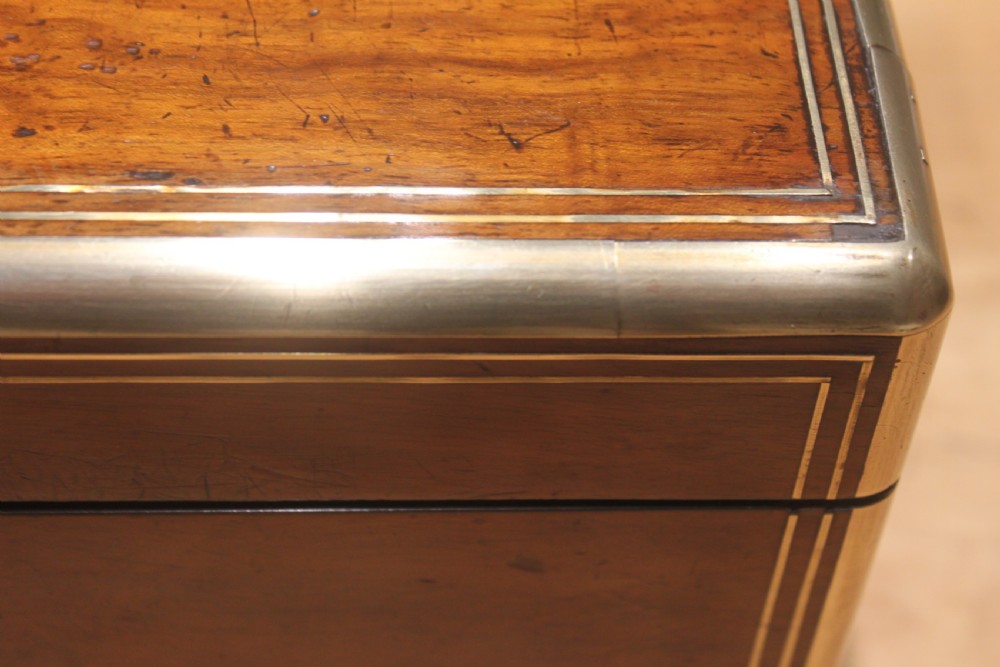 A closed Victorian writing slope crafted from figured walnut veneer featuring brass edging, line inlay, a brass cartouche, and a key inserted in the Bramah lock with a tassel. View V