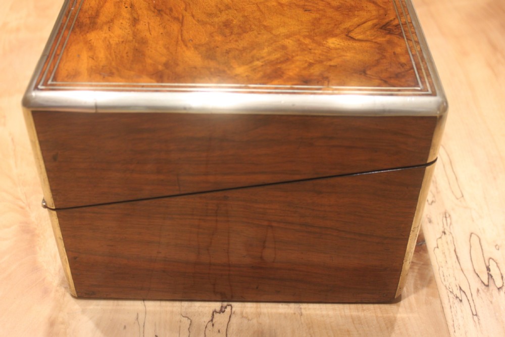 A closed Victorian writing slope crafted from figured walnut veneer featuring brass edging, line inlay, a brass cartouche, and a key inserted in the Bramah lock with a tassel. View VI