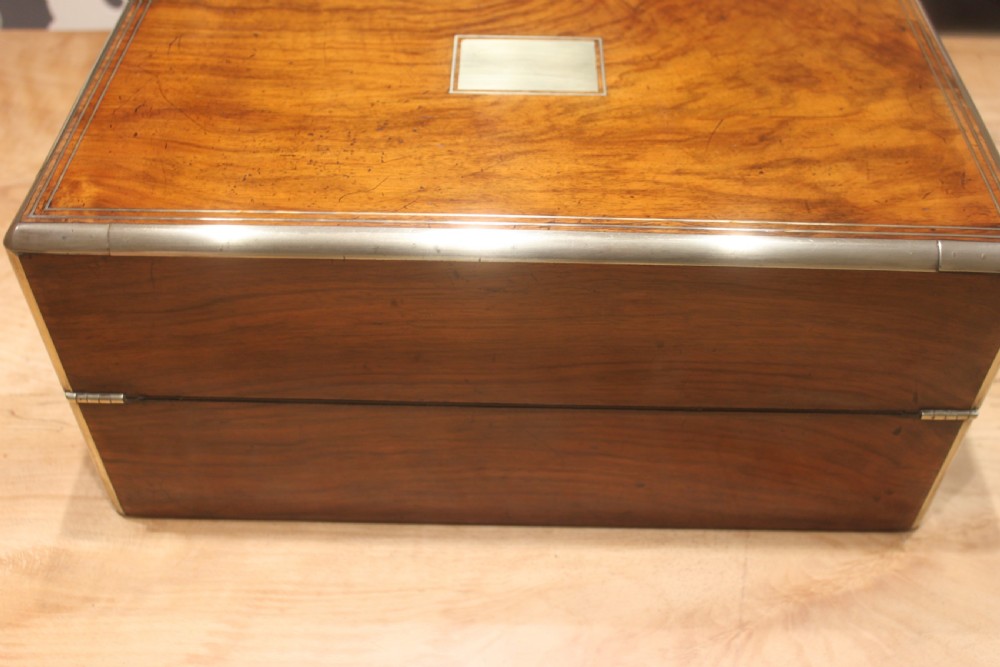 A closed Victorian writing slope crafted from figured walnut veneer featuring brass edging, line inlay, a brass cartouche, and a key inserted in the Bramah lock with a tassel. View VII