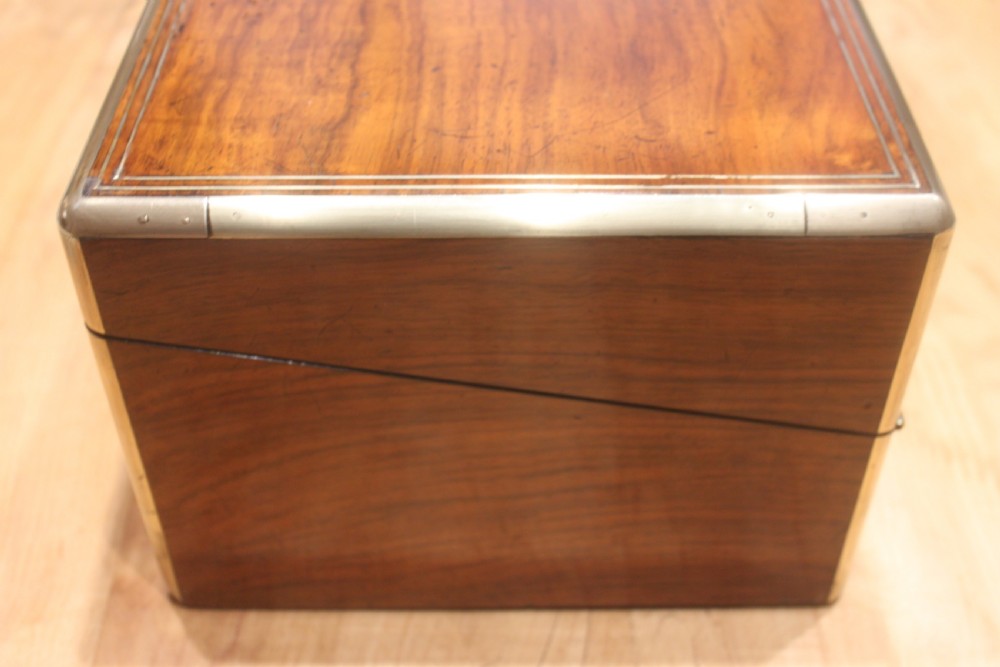 A closed Victorian writing slope crafted from figured walnut veneer featuring brass edging, line inlay, a brass cartouche, and a key inserted in the Bramah lock with a tassel. View VIII