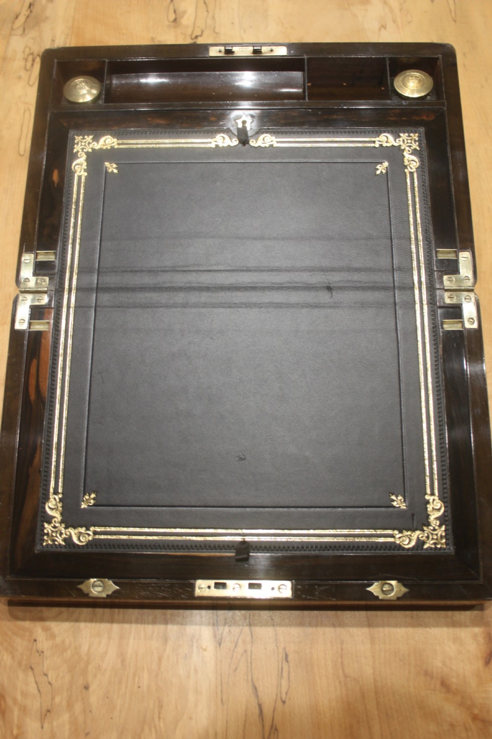 A closed Victorian writing slope crafted from figured walnut veneer featuring brass edging, line inlay, a brass cartouche, and a key inserted in the Bramah lock with a tassel. View IX