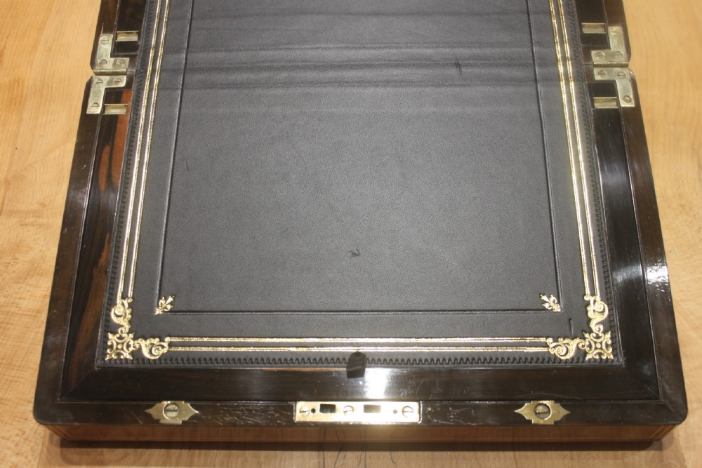 A closed Victorian writing slope crafted from figured walnut veneer featuring brass edging, line inlay, a brass cartouche, and a key inserted in the Bramah lock with a tassel. View X