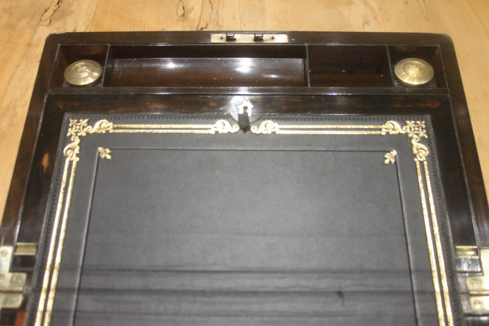 A closed Victorian writing slope crafted from figured walnut veneer featuring brass edging, line inlay, a brass cartouche, and a key inserted in the Bramah lock with a tassel. View XI