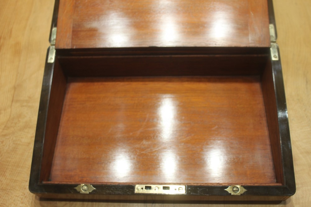 A closed Victorian writing slope crafted from figured walnut veneer featuring brass edging, line inlay, a brass cartouche, and a key inserted in the Bramah lock with a tassel. View XII