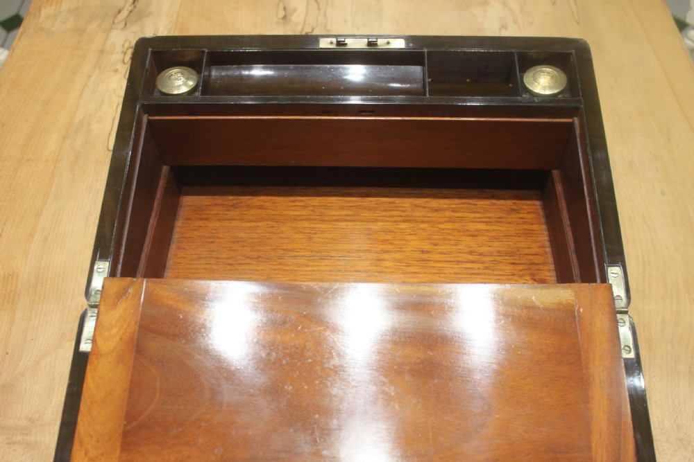 A closed Victorian writing slope crafted from figured walnut veneer featuring brass edging, line inlay, a brass cartouche, and a key inserted in the Bramah lock with a tassel. View XIII