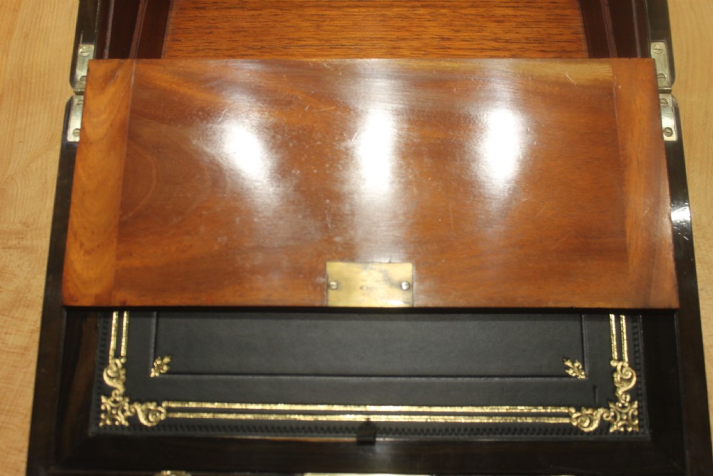 A closed Victorian writing slope crafted from figured walnut veneer featuring brass edging, line inlay, a brass cartouche, and a key inserted in the Bramah lock with a tassel. View XIV