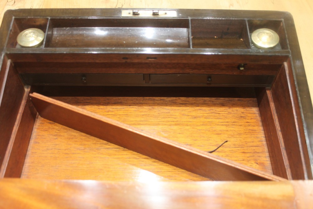 A closed Victorian writing slope crafted from figured walnut veneer featuring brass edging, line inlay, a brass cartouche, and a key inserted in the Bramah lock with a tassel. View XV