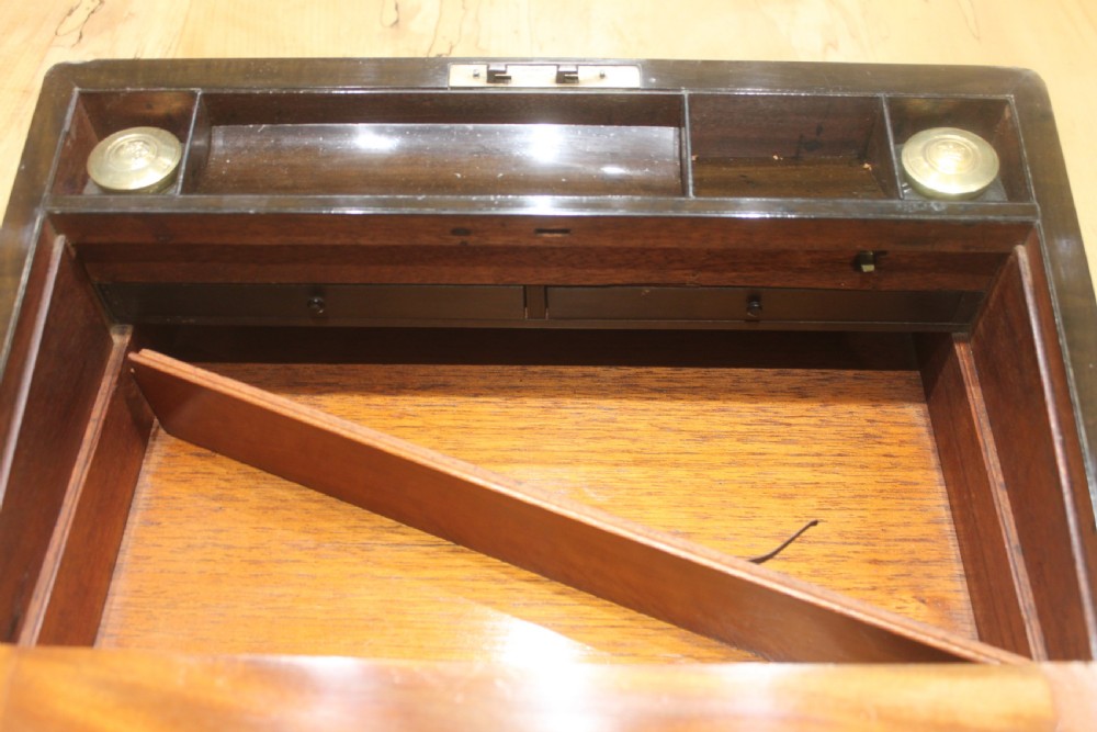 A closed Victorian writing slope crafted from figured walnut veneer featuring brass edging, line inlay, a brass cartouche, and a key inserted in the Bramah lock with a tassel. View XVI