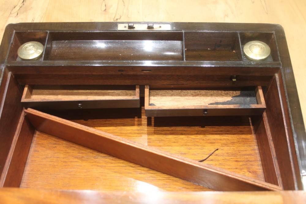 A closed Victorian writing slope crafted from figured walnut veneer featuring brass edging, line inlay, a brass cartouche, and a key inserted in the Bramah lock with a tassel. View XVII