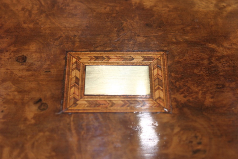 A rectangular Victorian burr walnut writing slope box featuring a domed lid, central inlaid cartouche, and a key inserted into the brass escutcheon. View II