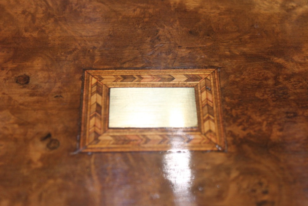 A rectangular Victorian burr walnut writing slope box featuring a domed lid, central inlaid cartouche, and a key inserted into the brass escutcheon. View III
