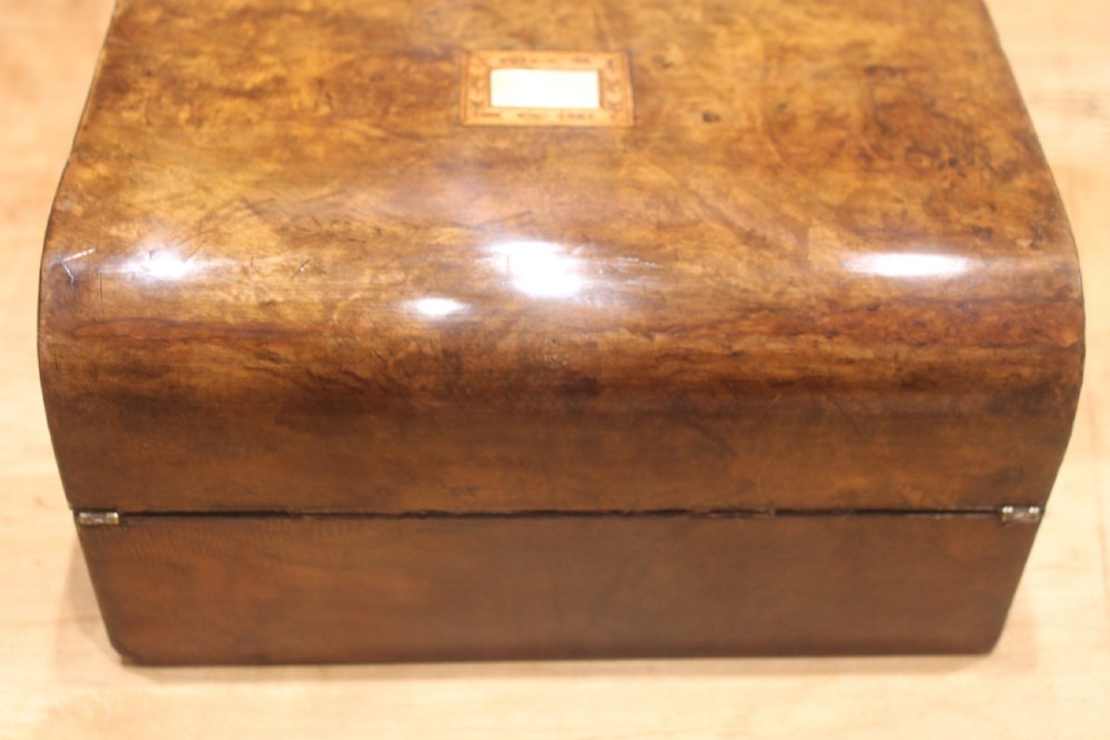 A rectangular Victorian burr walnut writing slope box featuring a domed lid, central inlaid cartouche, and a key inserted into the brass escutcheon. View VII