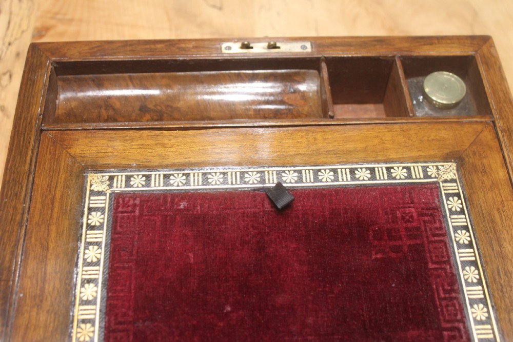 A rectangular Victorian burr walnut writing slope box featuring a domed lid, central inlaid cartouche, and a key inserted into the brass escutcheon. View X