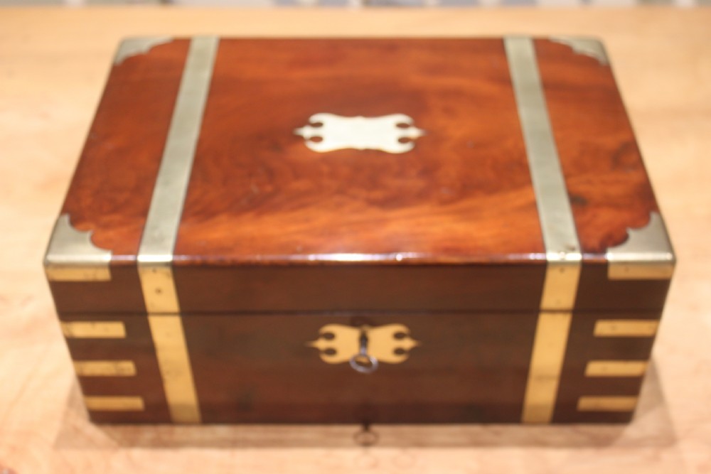 A closed mahogany campaign writing slope featuring brass corner brackets, brass banding, and a central brass cartouche with a key in the escutcheon.