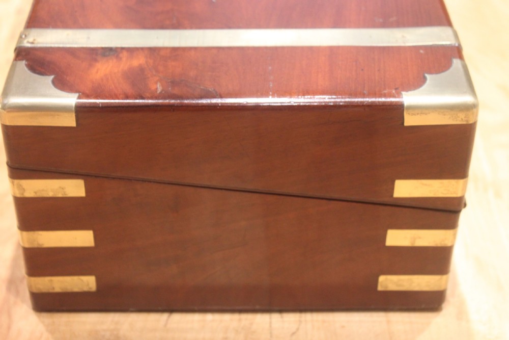 A closed mahogany campaign writing slope featuring brass corner brackets, brass banding, and a central brass cartouche with a key in the escutcheon. View V