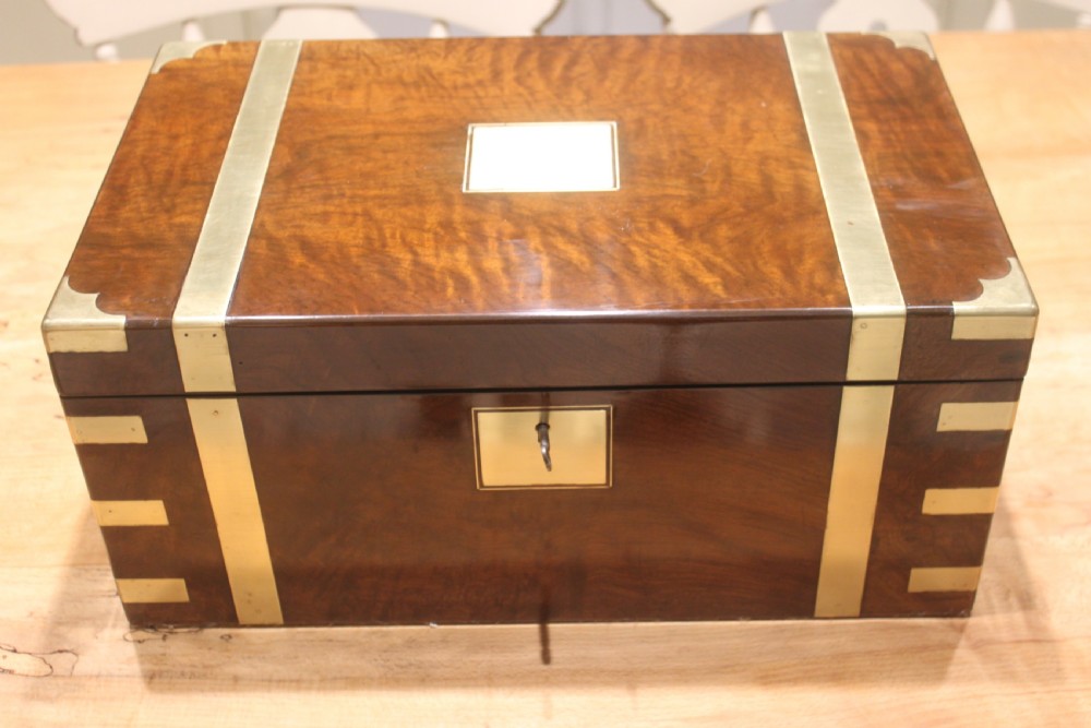 A rectangular figured walnut writing slope decorated with brass corner brackets, brass strapping, a blank central brass cartouche, and a keyhole escutcheon.