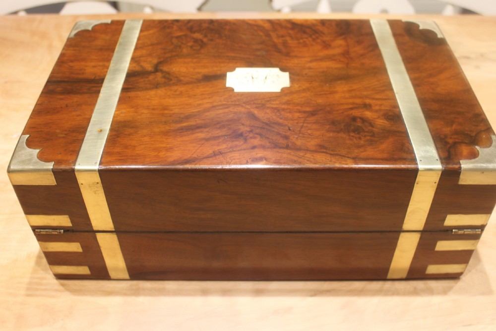 A closed Victorian figured walnut writing slope featuring protective brass straps, corner mounts, an inlaid central cartouche, and a key inserted into the lock. View IV