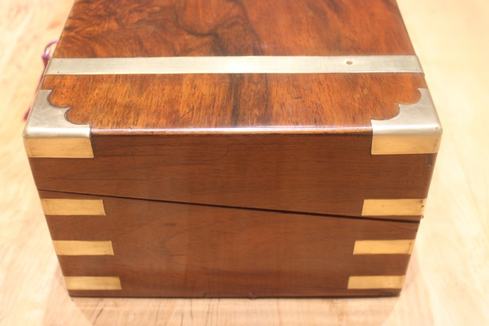 A closed Victorian figured walnut writing slope featuring protective brass straps, corner mounts, an inlaid central cartouche, and a key inserted into the lock. View V