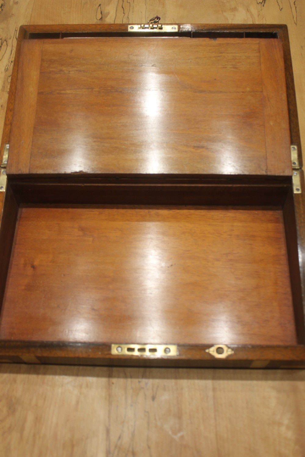 A closed Victorian figured walnut writing slope featuring protective brass straps, corner mounts, an inlaid central cartouche, and a key inserted into the lock. View VII
