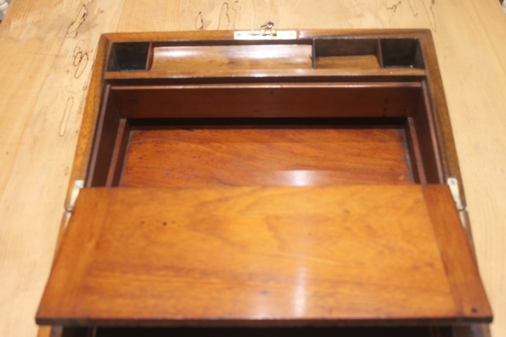 A closed Victorian figured walnut writing slope featuring protective brass straps, corner mounts, an inlaid central cartouche, and a key inserted into the lock. View VIII