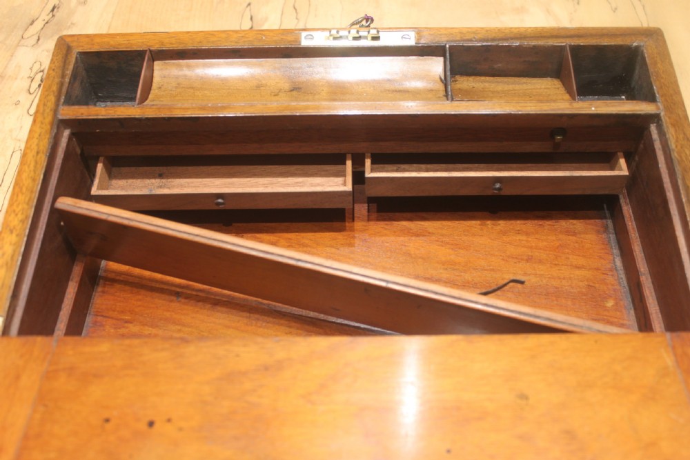A closed Victorian figured walnut writing slope featuring protective brass straps, corner mounts, an inlaid central cartouche, and a key inserted into the lock. View IX