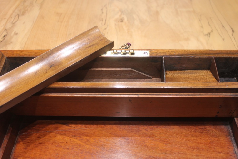 A closed Victorian figured walnut writing slope featuring protective brass straps, corner mounts, an inlaid central cartouche, and a key inserted into the lock. View X