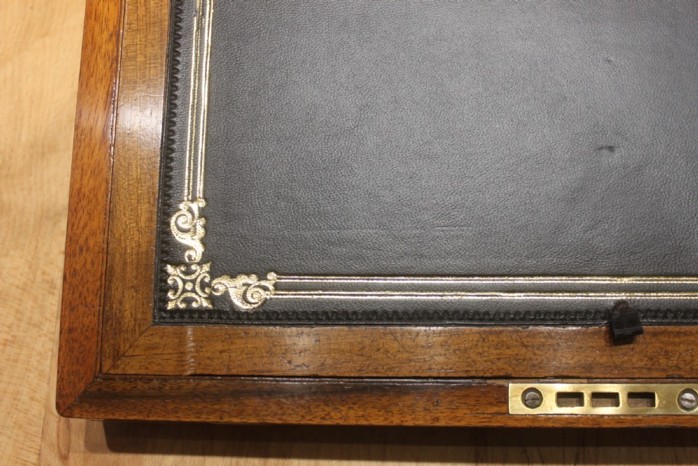 A closed Victorian figured walnut writing slope featuring protective brass straps, corner mounts, an inlaid central cartouche, and a key inserted into the lock. View XI