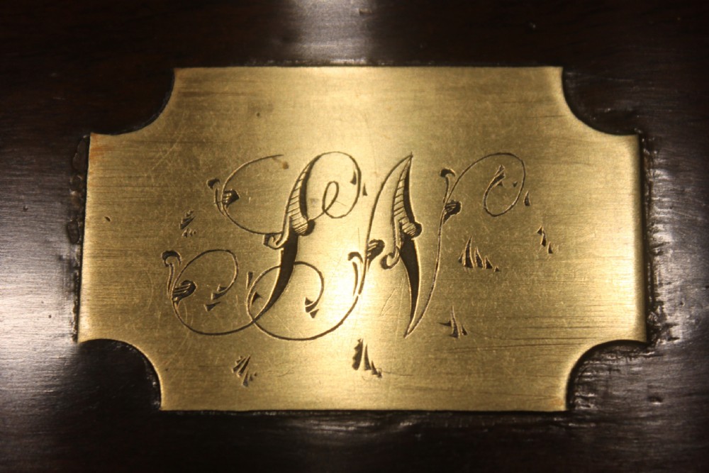 A closed Victorian figured walnut writing slope featuring protective brass straps, corner mounts, an inlaid central cartouche, and a key inserted into the lock. View XII