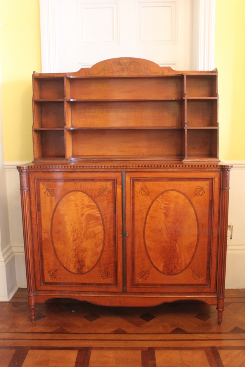 An antique Sheraton style satinwood cabinet with an open tiered shelving top unit and a lower two-door cabinet featuring oval inlaid marquetry panels. View II